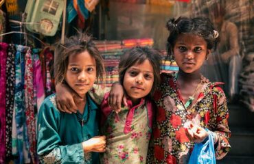 pexels-photo-27597369-27597369 A group of three children in vibrant traditional attire posing in Jalandhar market street.